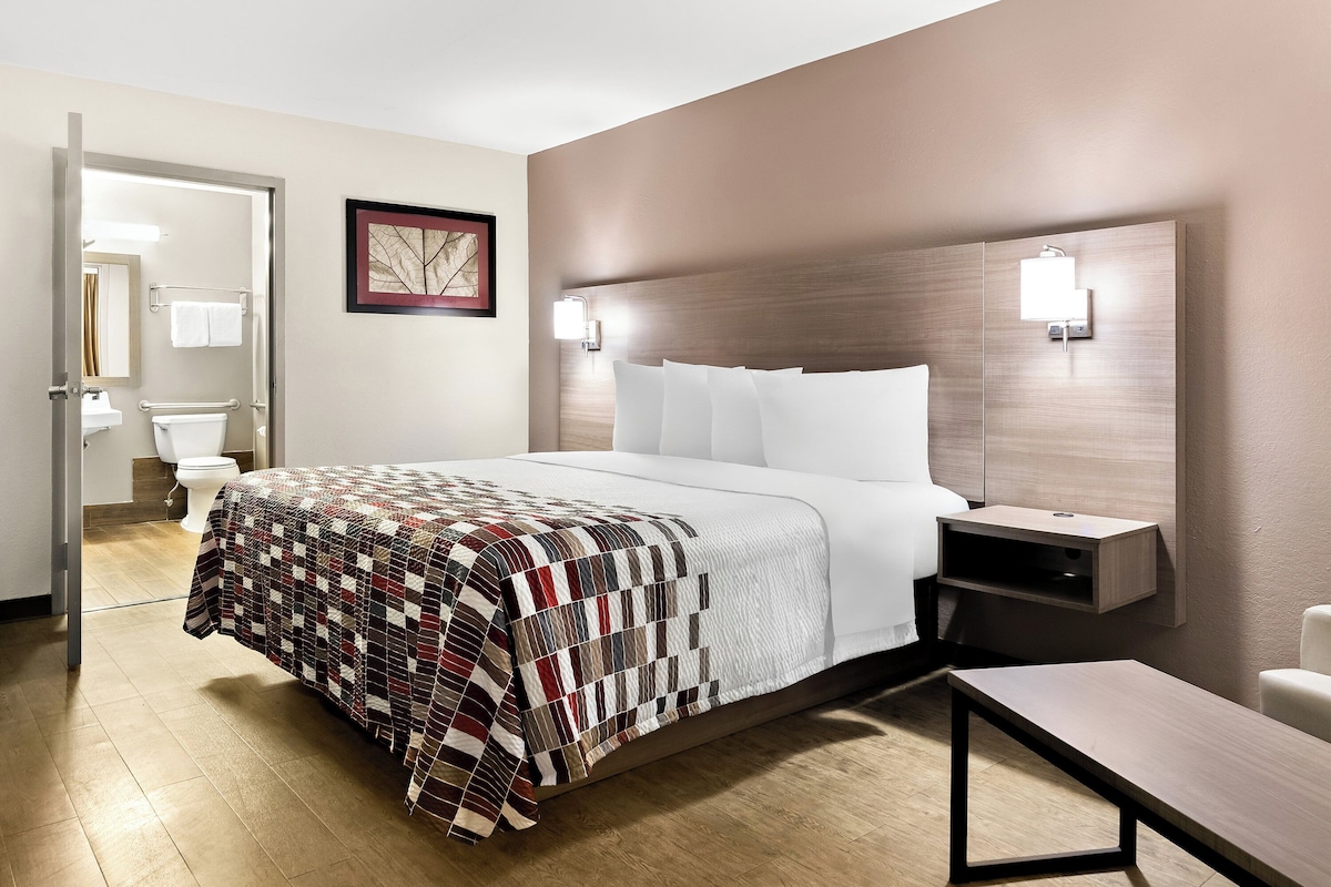 A hotel room with a bed, bedside table, and a view of the bathroom.