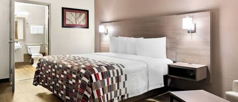 A hotel room with a bed, bedside table, and a view of the bathroom.