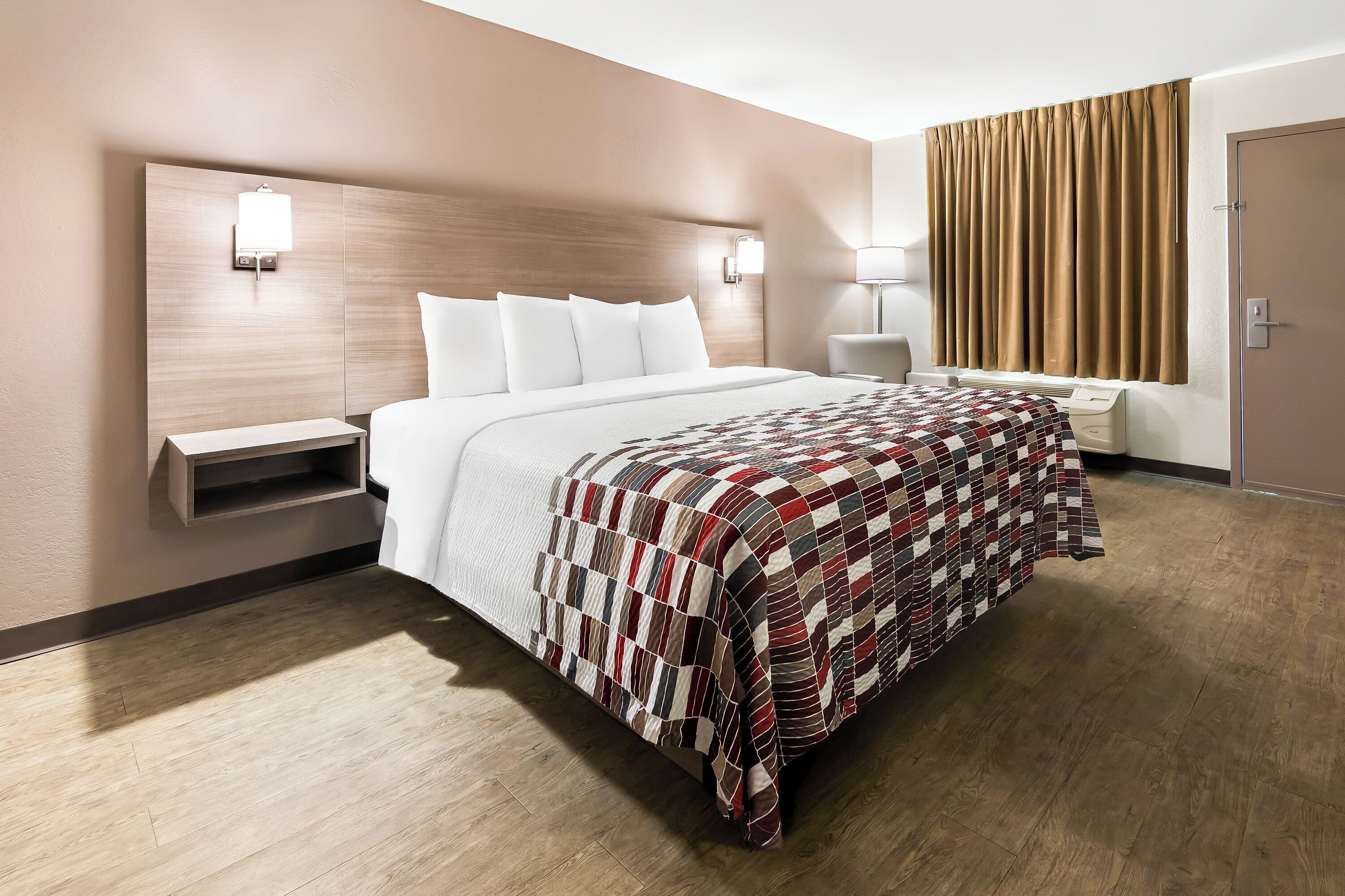 A hotel room with a large bed, a bedside table, a lamp, and a window with curtains.