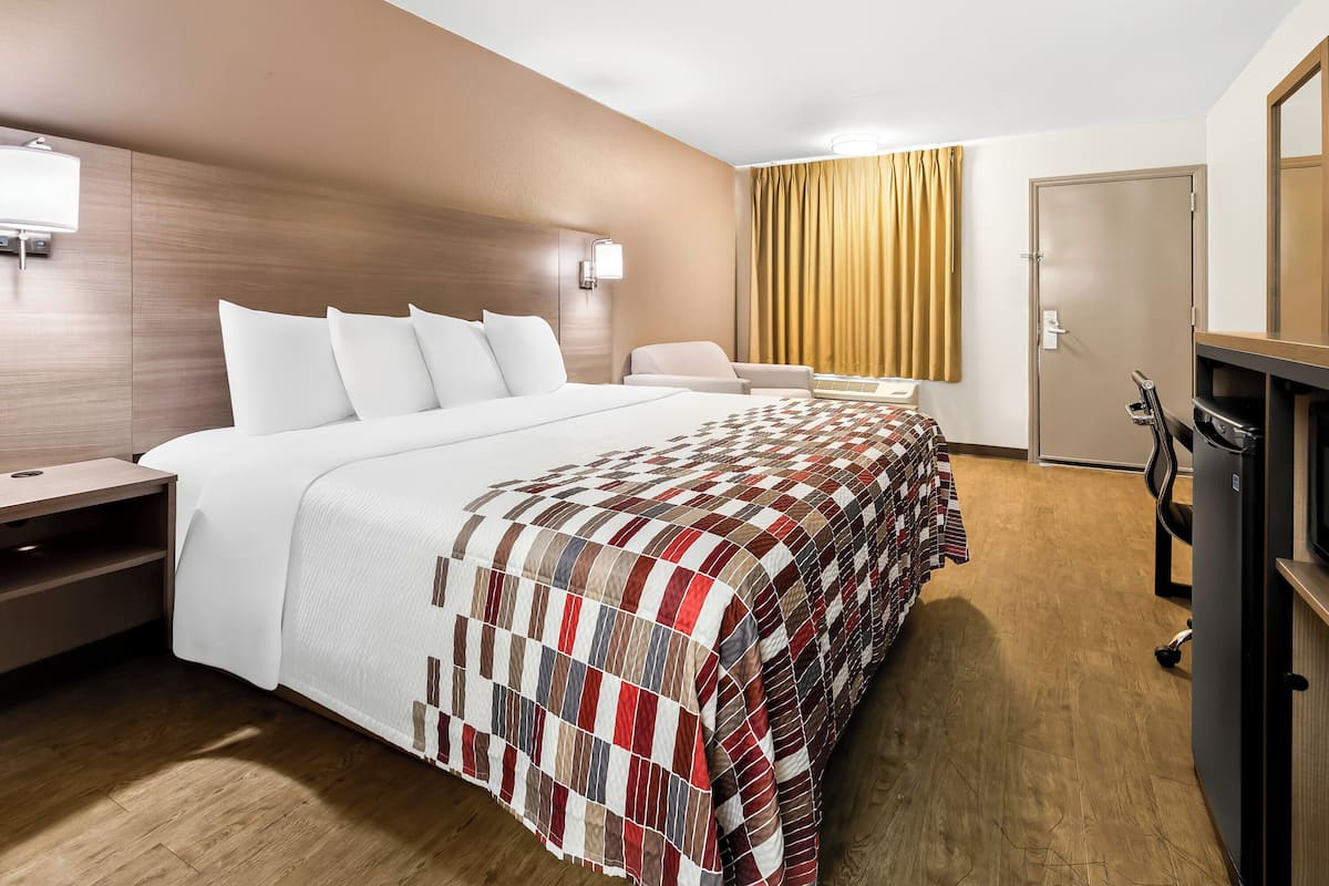 Een hotelkamer met een groot bed, een bureau, een stoel, een kledingkast en een raam met gordijnen.