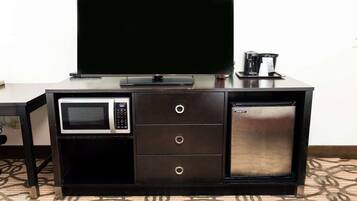 Una kitchenette compacta con microondas, refrigerador y un televisor de pantalla plana sobre un mueble de madera oscura.