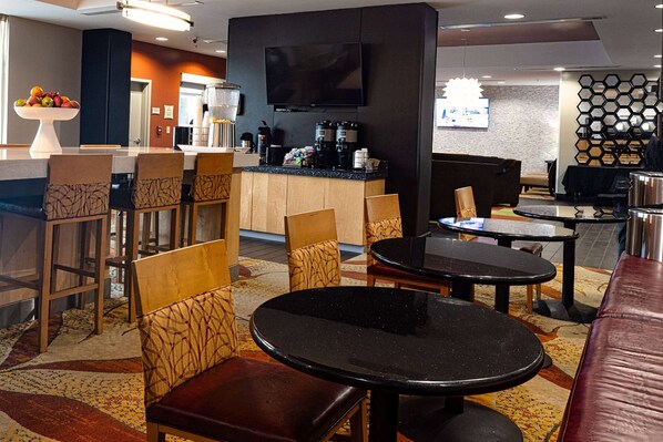 Un hall de hotel con una zona de bar, asientos y una televisión.