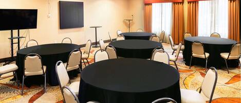 A conference room with multiple tables and chairs, a flat-screen TV, and a sound system.