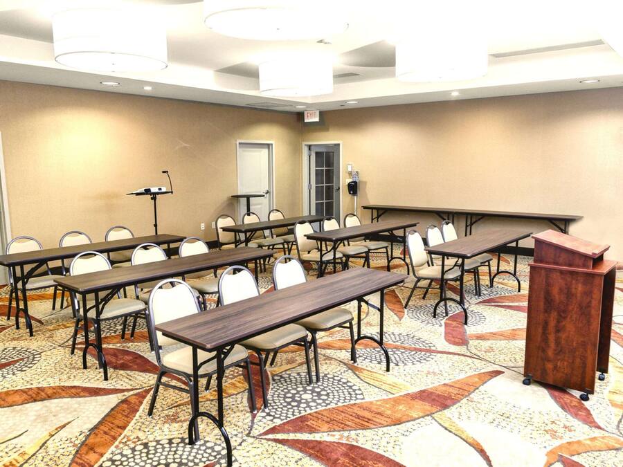 A conference room with multiple tables and chairs, a podium, and an exit sign.