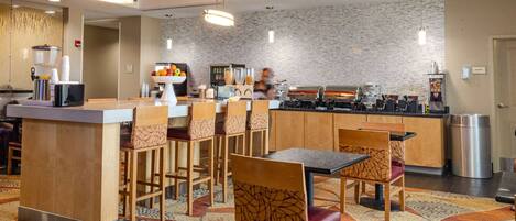 A hotel lobby with a central bar area, seating arrangements, and a kitchen in the background.