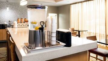 Una zona de cocina con dispensador de agua, tazas blancas apiladas y una máquina de café.