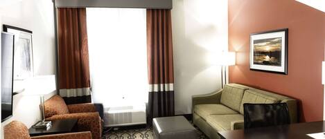 A hotel room with a sofa, a small table, a coffee table, a TV, and a picture on the wall.