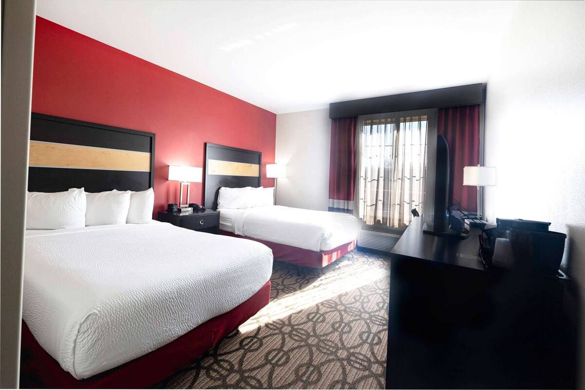 A hotel room with two beds, a desk, and a view of the outdoors.