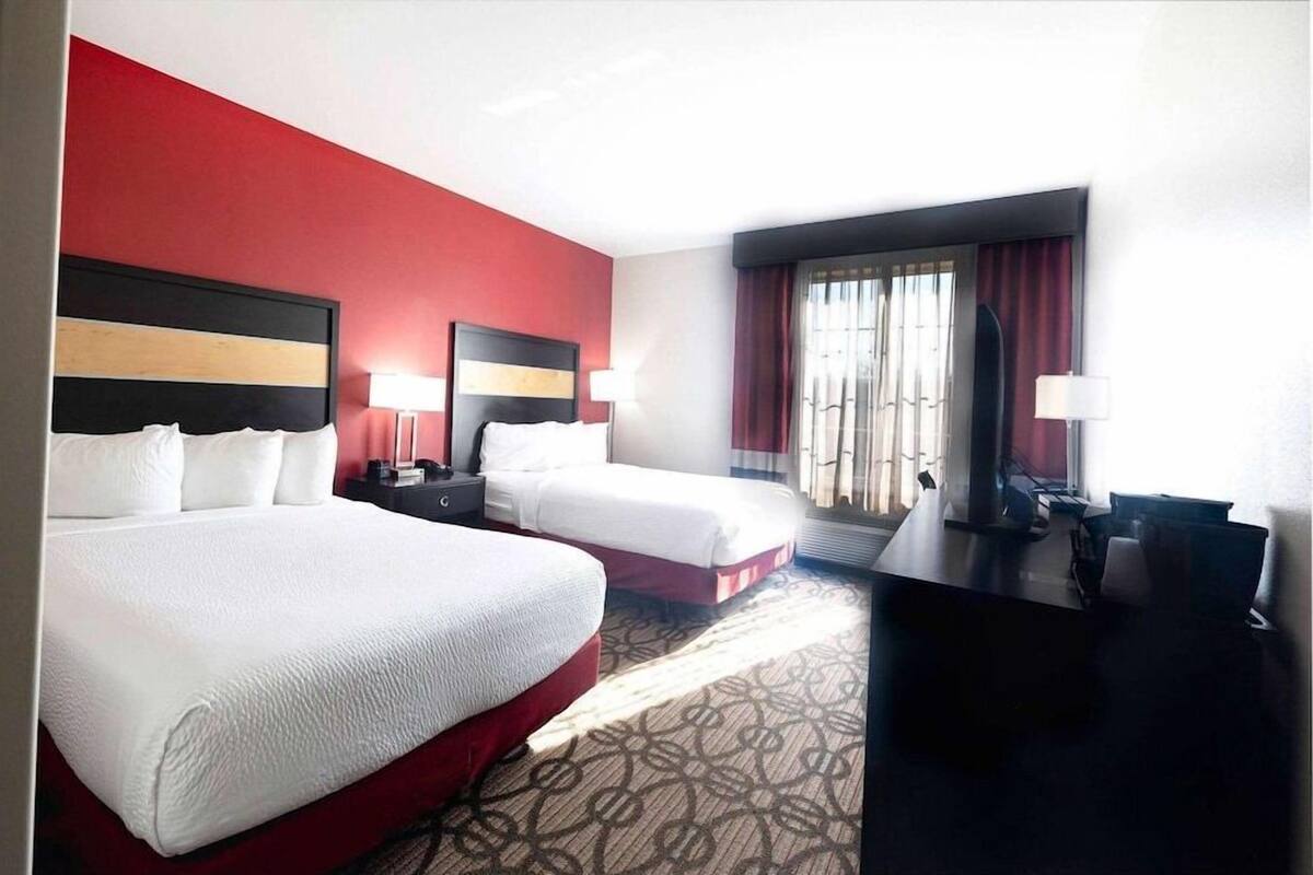 A hotel room with two beds, a desk, and a window with curtains.