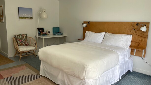 A neatly arranged bedroom with a large bed, a chair, a desk, and a wall-mounted lamp. - Lincolnville Motel (Lincolnville)