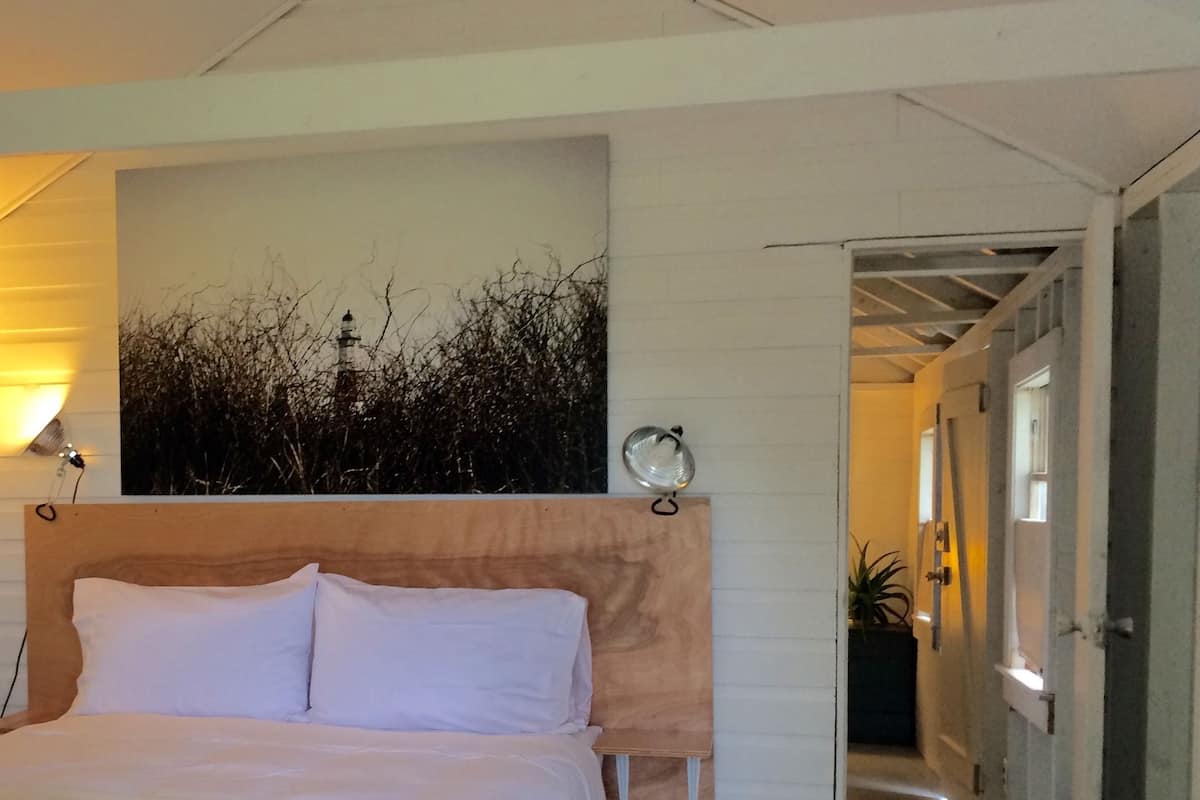A bedroom with a bed, a wall-mounted lamp, and a door leading to another room.