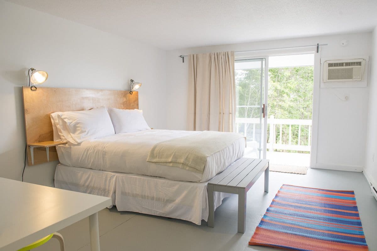 A bedroom with a bed, bedside tables, a bench, a colorful rug, and a balcony with curtains.