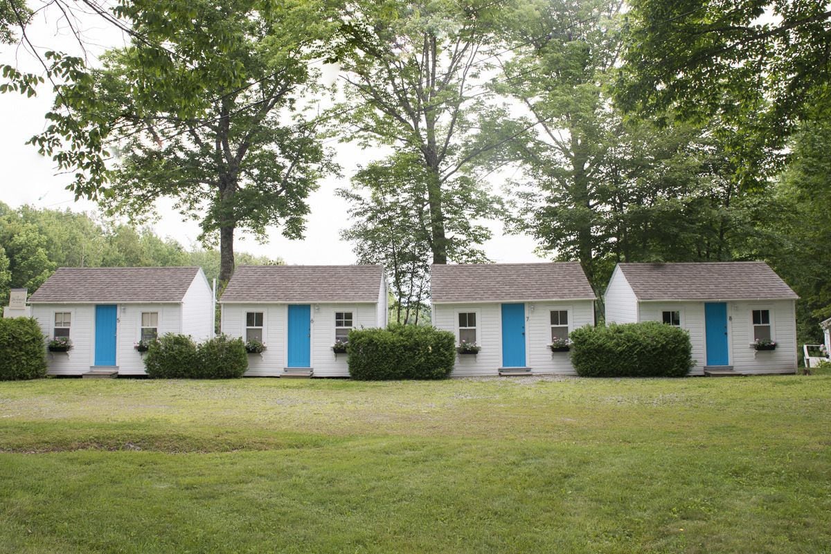 A row of white motel buildings with blue doors and windows, surrounded by green grass and trees.