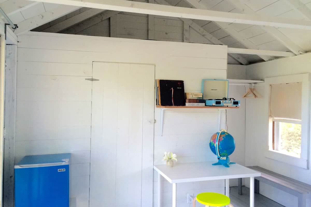 A room with a white door, a blue cabinet, a white table with a globe and a flower, and a window with a view.