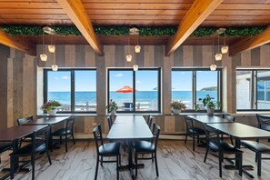 A restaurant with large windows offering ocean views, wooden ceiling beams, and potted plants. - Pilgrim Sands on Long Beach (Plymouth)