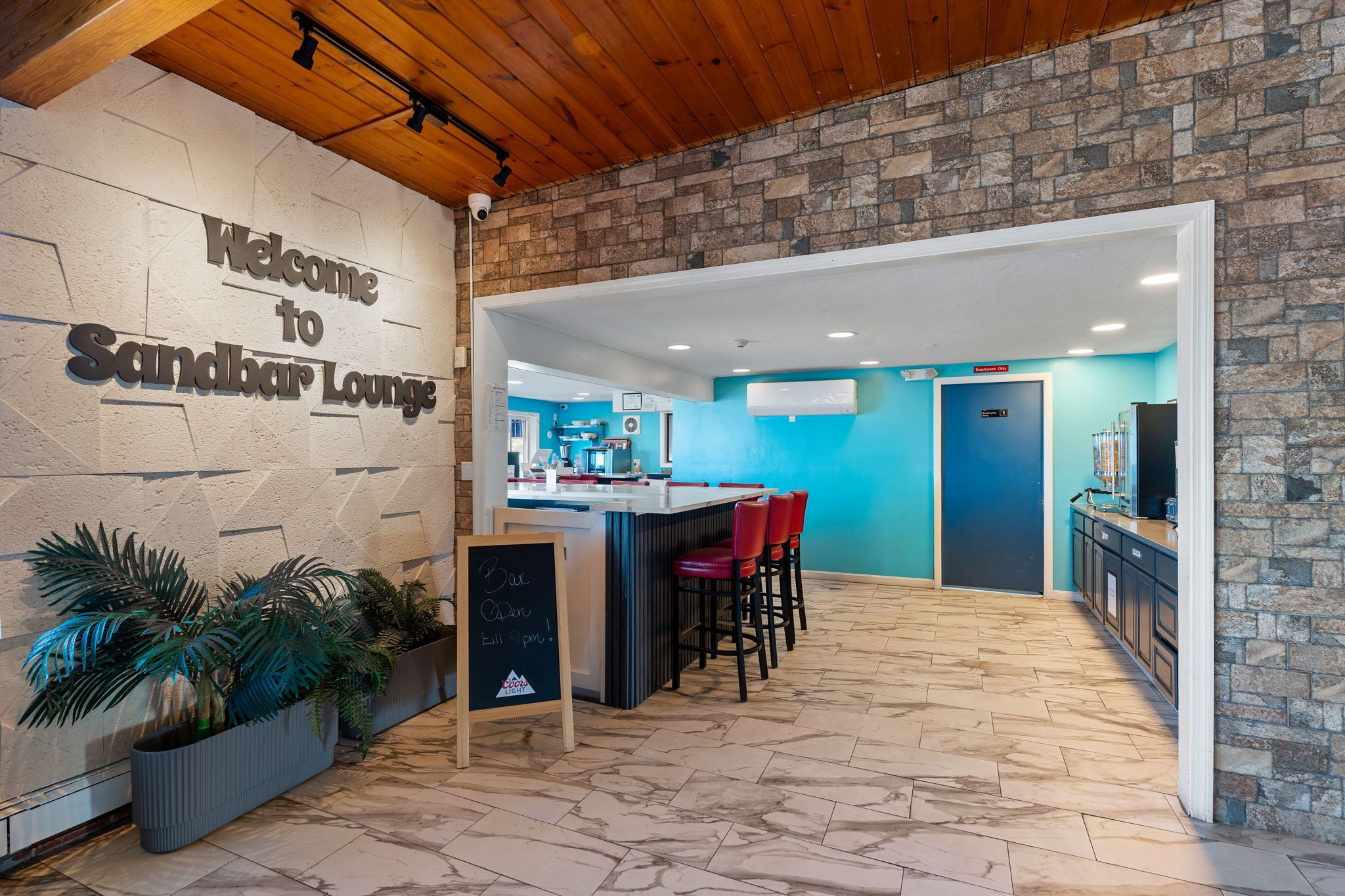 A modern lounge area with a stone wall, a bar counter, and red bar stools.