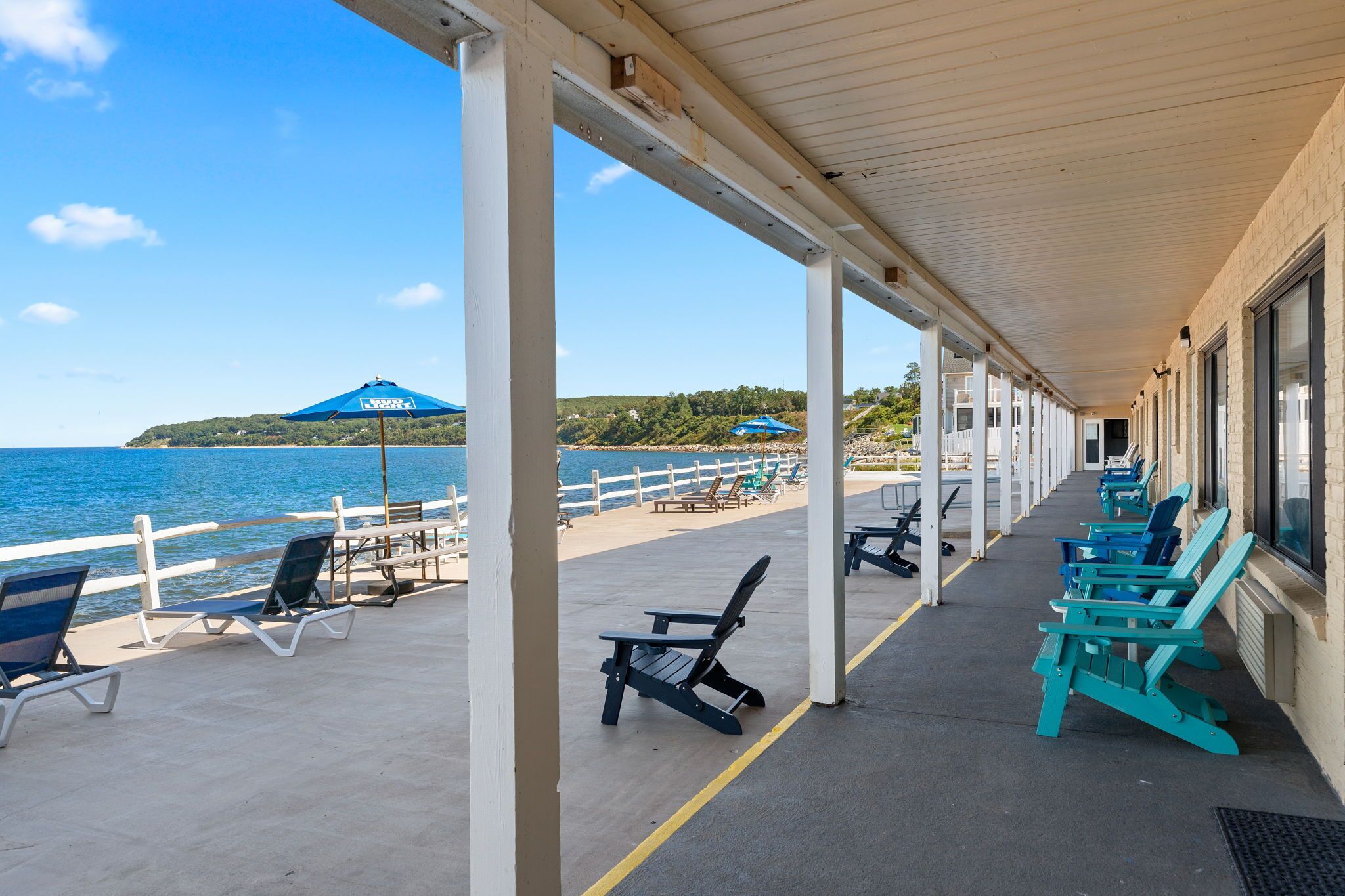 A covered outdoor seating area with chairs and umbrellas, overlooking a beach and the sea.