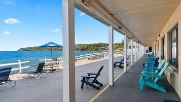 A covered outdoor seating area with chairs and umbrellas, overlooking a beach and the sea.