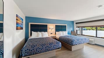 A modern hotel room with two beds, a large window, and a view of the outdoors.