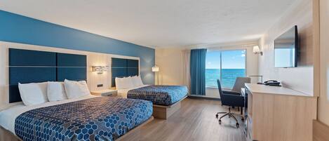 A hotel room with two beds, a desk, and a large window with a view of the sea.
