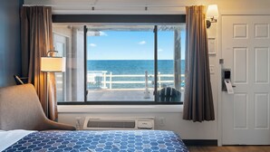 Ein Hotelzimmer mit Bett, Stuhl, Fenster mit Vorhängen, Meerblick und einer Tür.