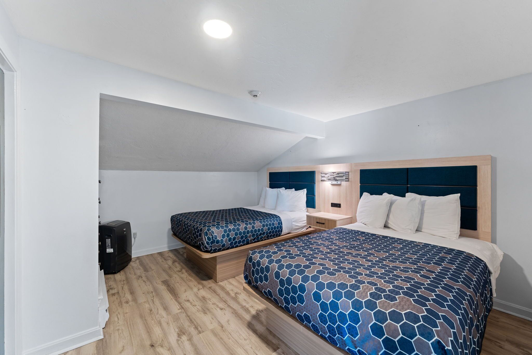 A bedroom with two beds, a ceiling light, and a small black suitcase.