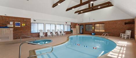 An indoor swimming pool with a brick wall, lounge chairs, and a ceiling with exposed beams.