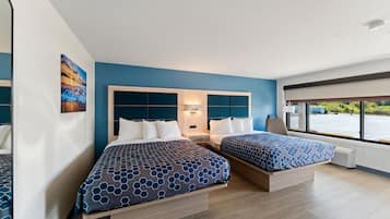 A hotel room with two beds, a large window, and a view of the outside.