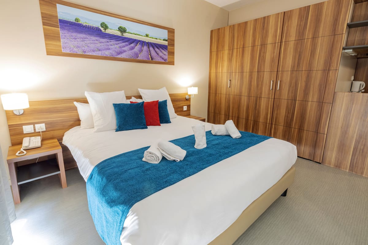 Une chambre d’hôtel avec un grand lit, une armoire en bois et un tableau représentant des champs de lavande.