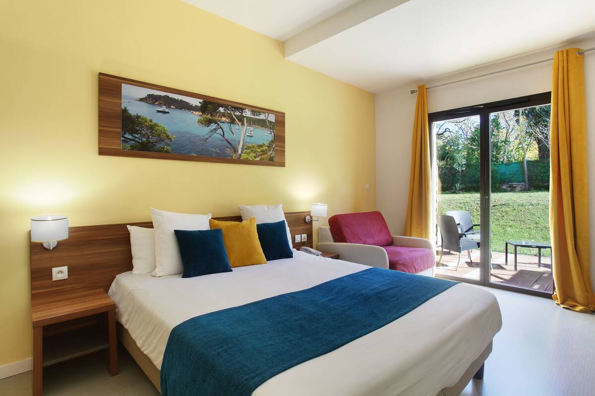Une chambre d’hôtel avec un grand lit, un tableau au mur, une chaise et une vue sur l’extérieur.