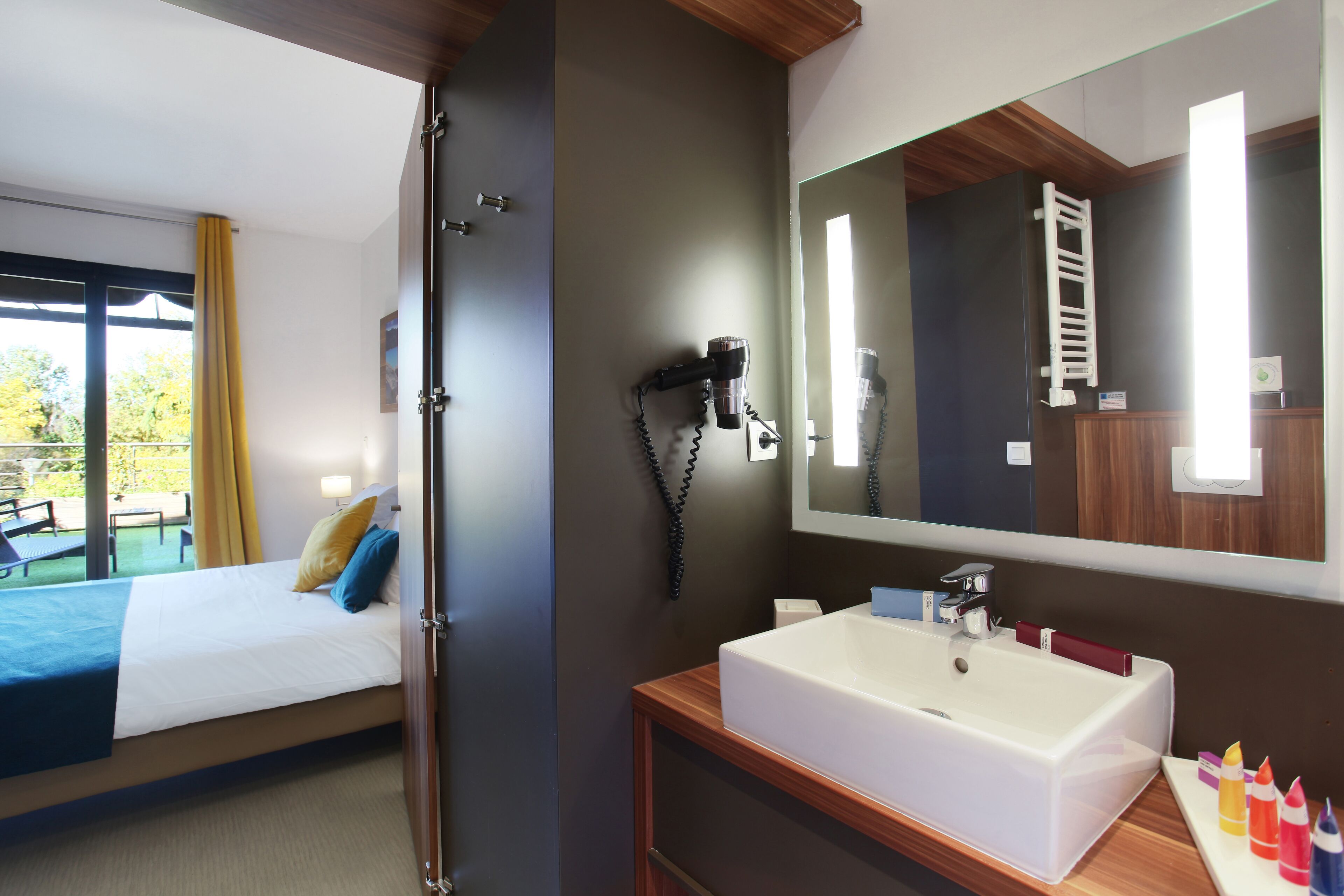 Habitación de hotel con cama, baño con un espejo grande, lavamanos y artículos de aseo.