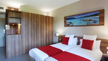 A hotel room with a large bed, a wooden wardrobe, a painting of a beach, and a nightstand with a lamp.