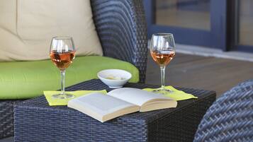 A wicker table with two wine glasses, a bowl of snacks, and an open book.