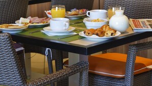 A breakfast buffet with various food items and beverages, wicker chairs, and a wooden wall with a logo. - Residence Suite Home Aix en Provence (Bouc-Bel-Air)