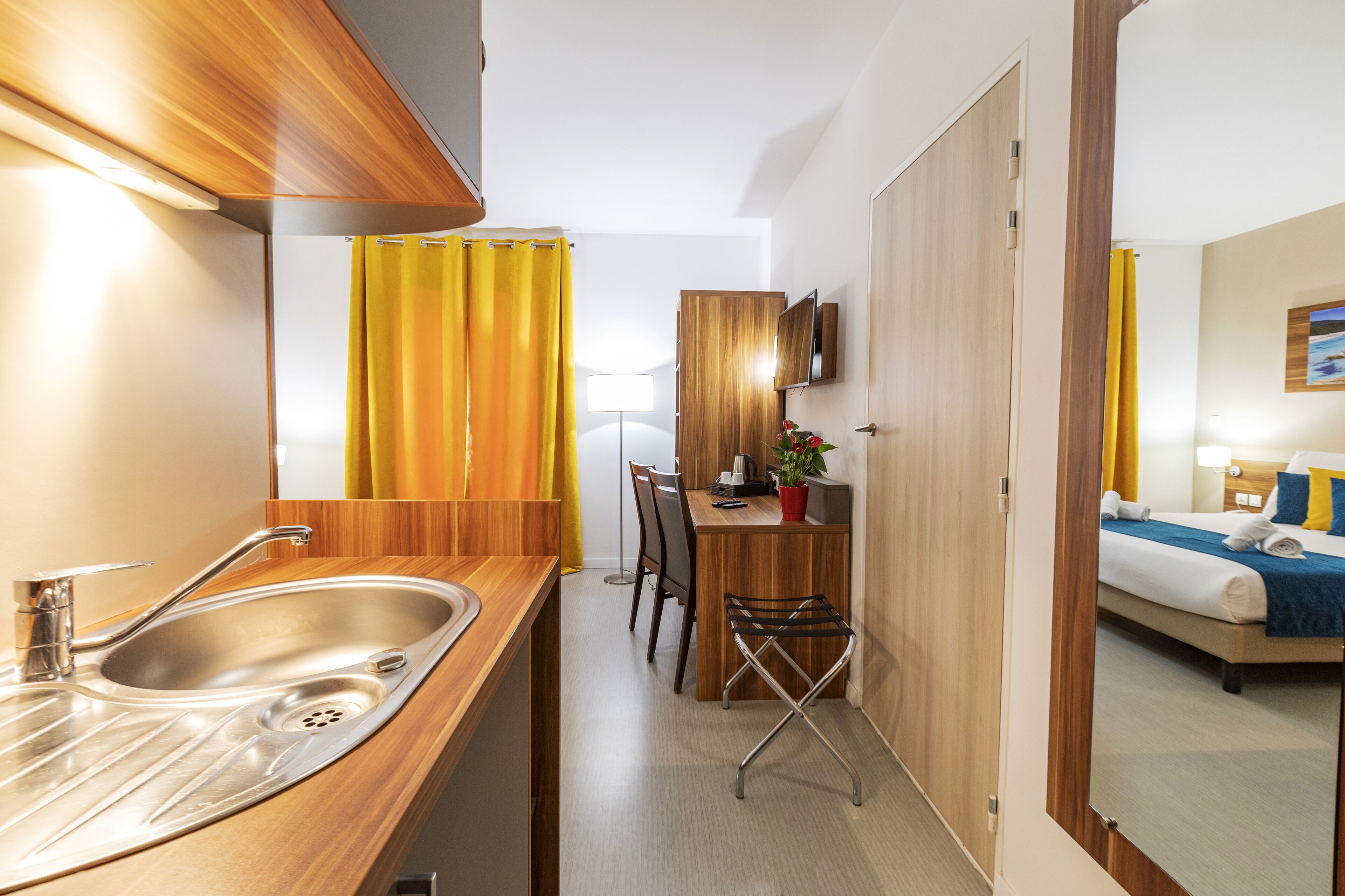 A compact hotel room with a kitchenette, a dining area, and a bed.