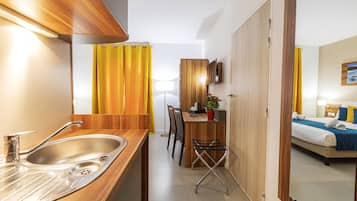 A compact hotel room with a kitchenette, a dining area, and a bed.