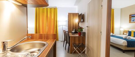 A compact hotel room with a kitchenette, a dining area, and a bed.
