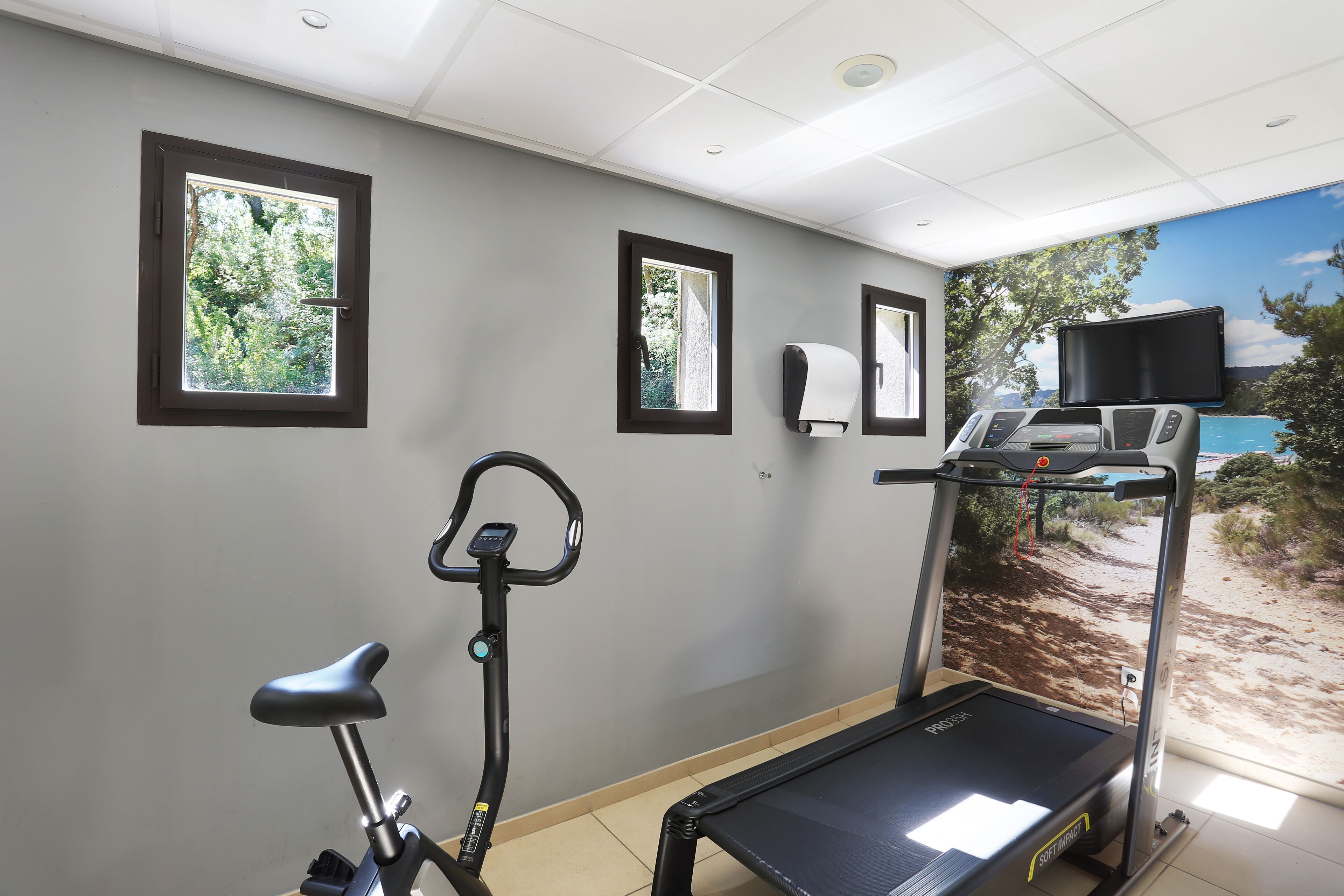 A gym with a treadmill, stationary bike, and a wall-mounted TV.