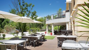 An outdoor patio area with tables and chairs, a covered seating area, and a building with a balcony. - Residence Suite Home Aix en Provence (Bouc-Bel-Air)