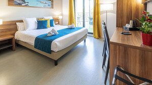 A hotel room with a bed, a desk, a chair, a potted plant, and a view of the outdoors. - Residence Suite Home Aix en Provence (Bouc-Bel-Air)
