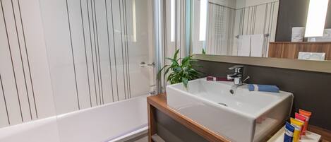 Un bagno moderno con una vasca da bagno bianca, un mobile bagno in legno con un lavandino grande e uno specchio sopra il lavandino.
