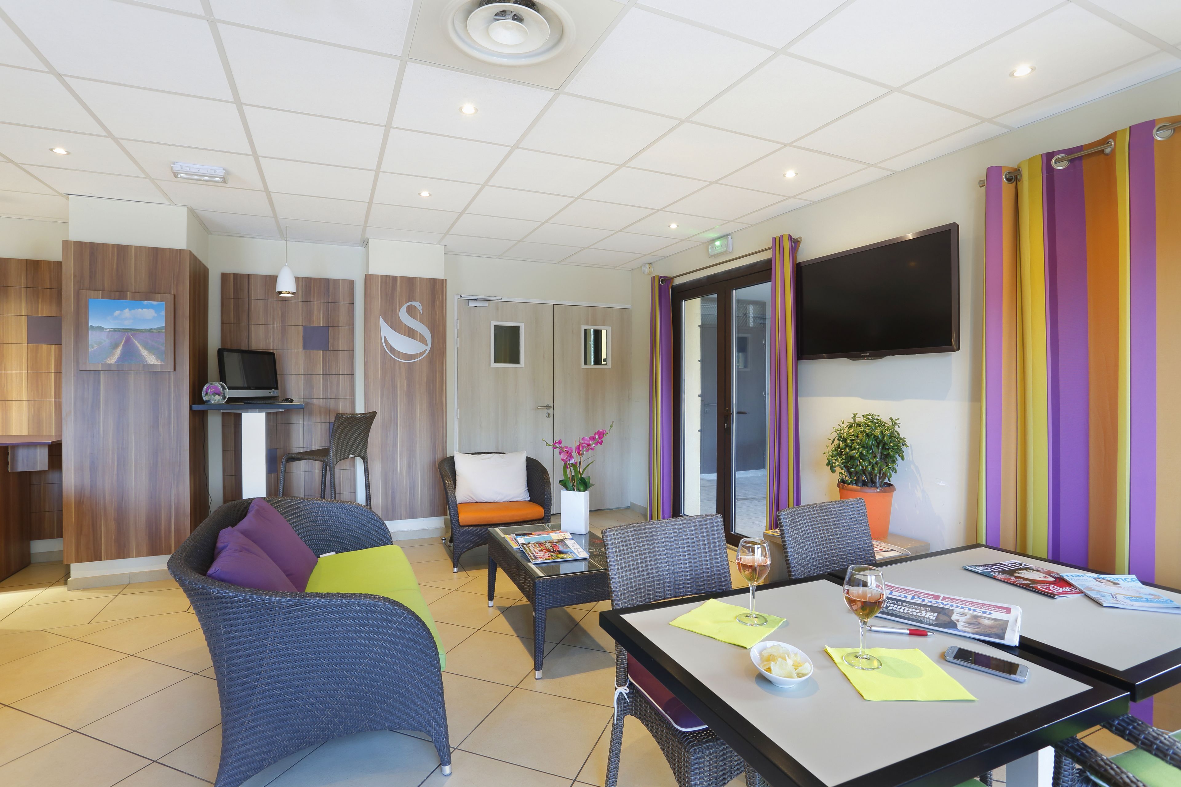 Une chambre d’hôtel moderne dotée d’un coin repas, d’une télévision et d’un mur rayé aux couleurs vives.
