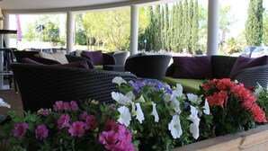 A covered outdoor seating area with wicker furniture and cushions, surrounded by a variety of flowers. - Residence Suite Home Aix en Provence (Bouc-Bel-Air)