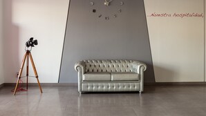A modern room with a grey sofa, a wall-mounted clock, and a tripod with a camera. - Alix Boutique (Arteixo)