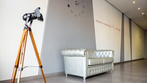 A modern interior with a camera on a tripod, a clock on the wall, and a tufted sofa. - Alix Boutique (Arteixo)