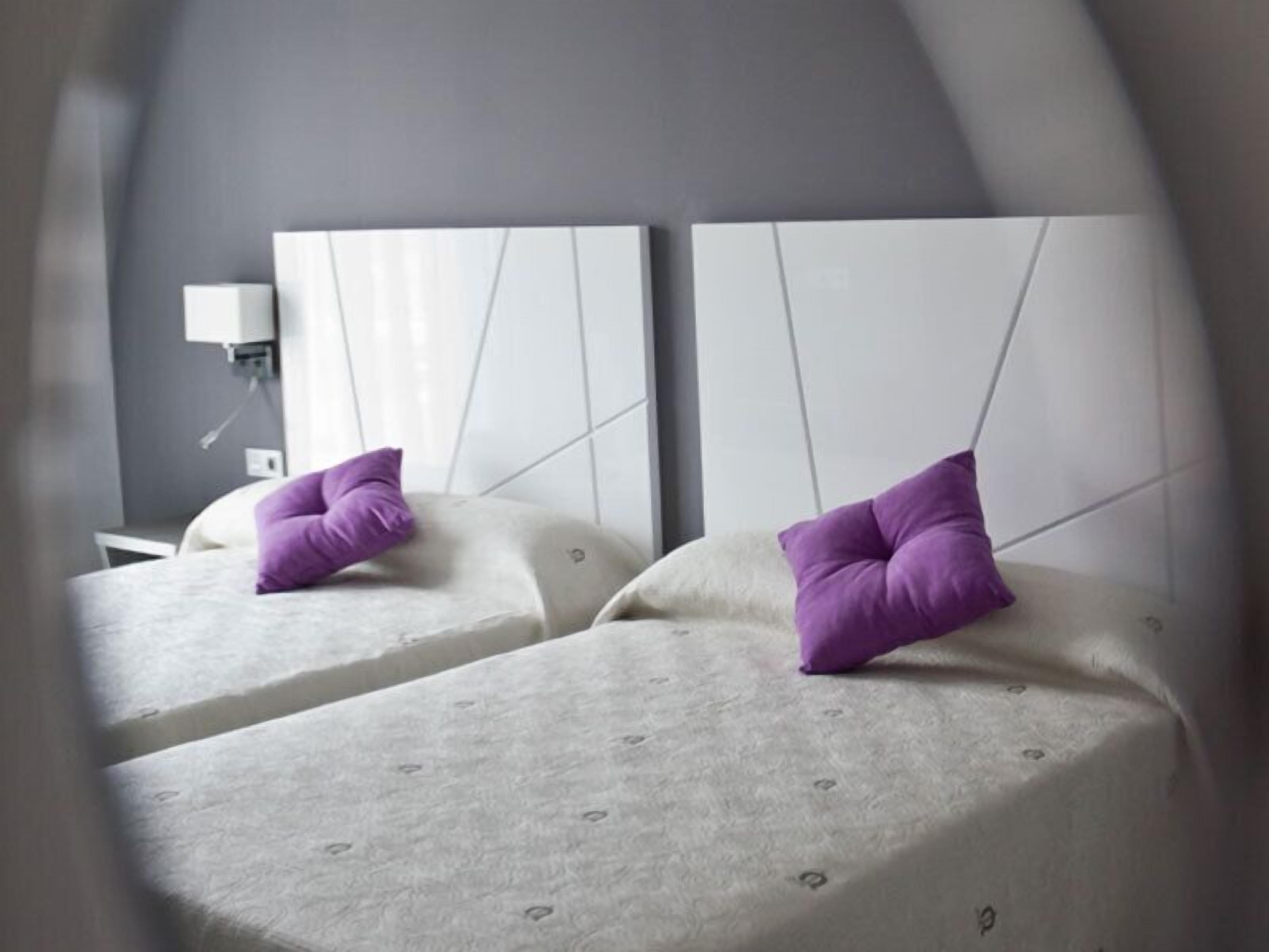 A modern hotel room with two beds, each with a white headboard and a purple pillow.