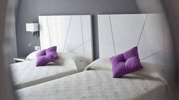 A modern hotel room with two beds, each with a white headboard and a purple pillow.