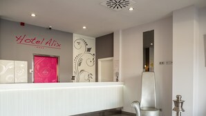 A hotel reception area with a modern design, including a reception desk, a chair, and a decorative wall with a logo. - Alix Boutique (Arteixo)