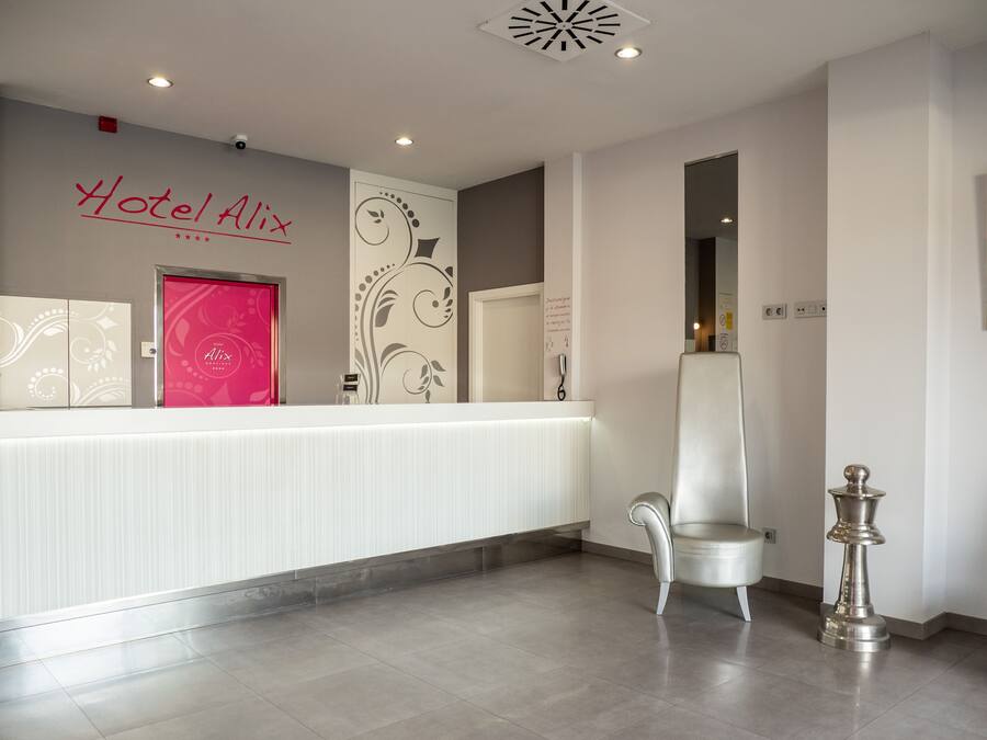 Zona de recepció d'hotel amb un disseny modern, incloent un taulell de recepció, una cadira i una paret decorativa amb un logotip.