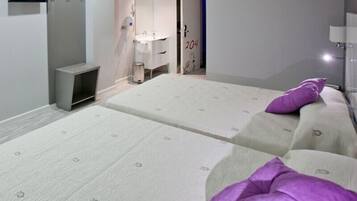 Habitación de hotel con dos camas, baño con espejo y lavamanos, y televisor montado en la pared.